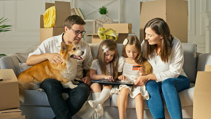 A Happy Family Uses a Laptop for Online Shopping, Sitting on the Couch at Home. Buying by the Internet. A Familly Sitting With a Cute Dog on the Couch at Home. Purchase Confirmation by the Internet