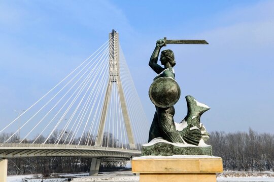Statue of Mermaid (Polish: Warszawska Syrenka) symbol of Warsaw by the Vistula river on the background of Swietokrzyski Bridge. Winter time in Warsaw, Poland. 