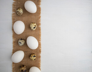 White chicken and quail eggs on a linen napkin on a white wooden background with space for text. Easter, holiday.