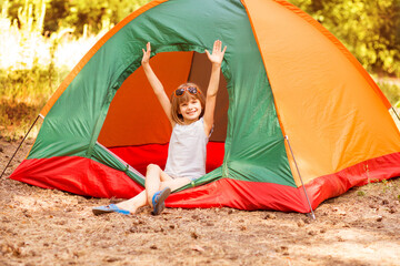 happy child girl in camp tent enjoy forest holidays with hands up.