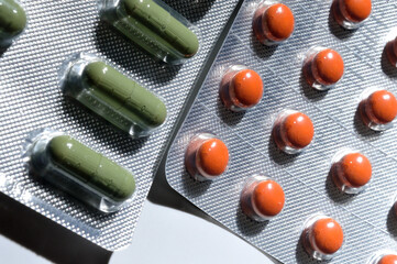 orange and green pills in a foil blister lie on a light background. large iplan. view from above