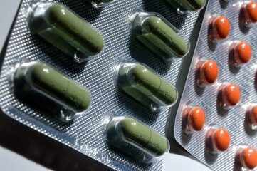 orange and green pills in a foil blister lie on a light background. large iplan. view from above