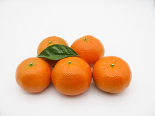 Five orange fresh tangerines and a green leaf on a white background.