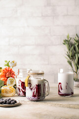 Bilberry or blueberry milkshake in glass bottle with fresh berries in ceramic plate and beautiful flowers on background.Healthy cocktail with vegan milk.