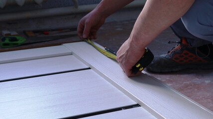 taking measurements on a light wooden canvas lying on the floor when installing metal fasteners using a tape measure in the hands of a carpenter, assembling a door frame on the floor in a room