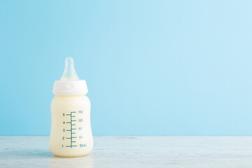 Bottle of white milk on wooden table at light blue wall background. Baby feeding concept. Pastel color. Closeup. Empty place for text. Front view.
