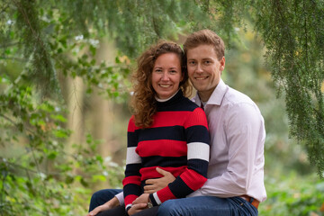 Beautiful enamored young couple sitting on a tree trunk in the forest. Facial expression is in love. In half body