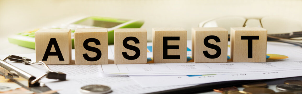 ASSEST inscription on the texture of wooden cubes. A business man holds a cube in his hand. An inscription on a financial, business or economic theme.