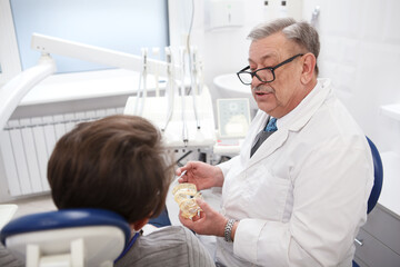 Obraz premium Elderly male dentist working at his clinic, talking to the patient