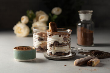 Classic italian dessert-Tiramisu in glasses with savoyardi cookies,mascarpone,cream liqueur and cocoa,with gentle flowers on background.Close-up.