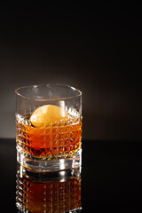 Elegant chrystal glass of Whiskey with whiskey ice ball on black with reflection.Close-up of noble acoholic drink.Minimalistic style.