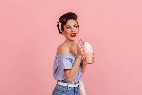 Amazed beautiful girl posing with milkshake. Trendy young woman enjoying cocktail on pink background.