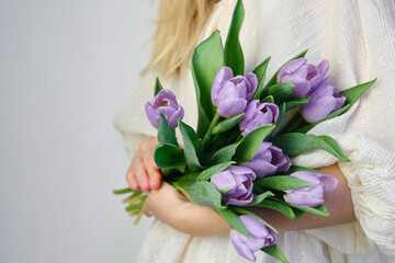 Happy woman holds purple tulips in her hands. Florist girl gathered a bouquet. Beautiful lavender flowers. Blossom petal. Gift for the holiday celebration, springtime mood. Romantic surprise