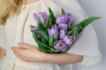 Happy woman holds purple tulips in her hands. Florist girl gathered a bouquet. Beautiful lavender flowers. Blossom petal. Gift for the holiday celebration, springtime mood. Romantic surprise