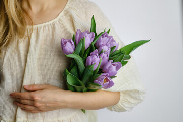 Obraz na płótnie Canvas Happy woman holds purple tulips in her hands. Florist girl gathered a bouquet. Beautiful lavender flowers. Blossom petal. Gift for the holiday celebration, springtime mood. Romantic surprise