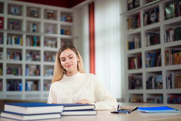 Portrait of clever student with open book reading it in college library.