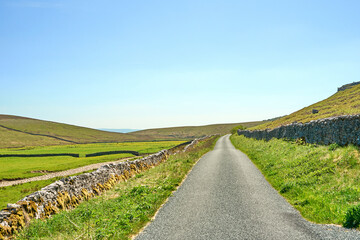 An empty straight, rural road disappearing to the horizon, surrounded by green meadows in the...