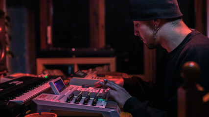 A producer in his studio, creating beats with his drum machines. Under red lights.
