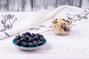Fresh blueberries in a glass bowl and muesli on a white wooden table in rustic style, close-up, horizontal, copy space