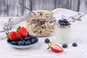 Healthy breakfast with homemade yoghurt and fresh strawberries and blueberries, muesli on a white wooden table in rustic style, close up, horizontal