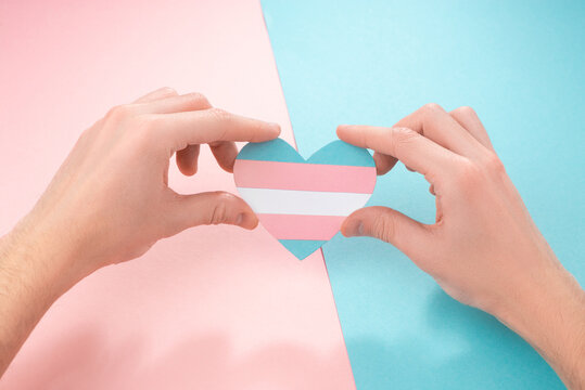 Two hands holding a paper heart with transgender pride flag