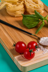 cherry tomatoes, basil, pasta and flour on bamboo board