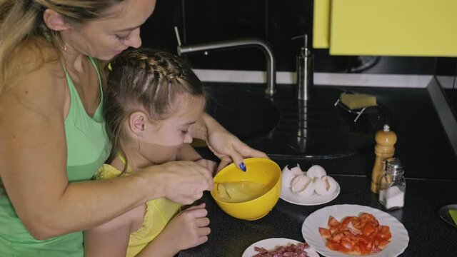 Mother teaching daughter smart girl learning to cook. Young mistress children to cook a Neapolitan egg fried omelette from salame affumicato sausage. Modern Built In Kitchen Appliances.
