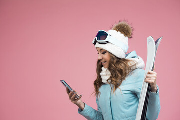 young woman with skis uses a smartphone to plan her ski runs. Winter holidays at a ski resort
