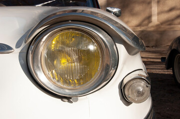 Headlight of an old white car in close-up