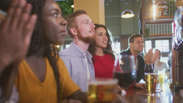 Group of disappointed customers in sports bar watching sporting event on TV as team lose - shot in slow motion