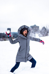 Fototapeta na wymiar Beautiful active young woman having a snowball fight in Montreal, she is happy and screaming, city in background