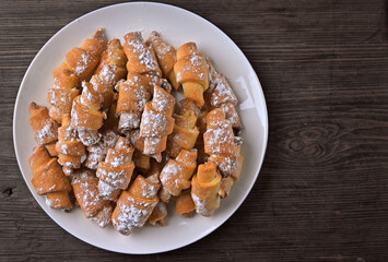 cottage cheese bagels in powdered sugar lie on a white plate side view on a wooden round section of birch