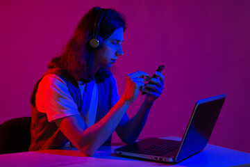 Student or programmer at a laptop, portrait in neon tinting. Funny guy geek writes code.