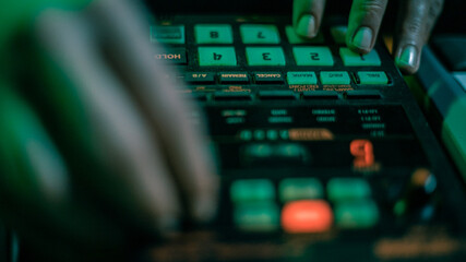 The hands of an artist creating music with his drum machines under green light.