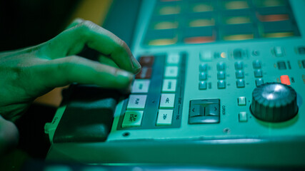 The hands of an artist creating music with his drum machines under green light.
