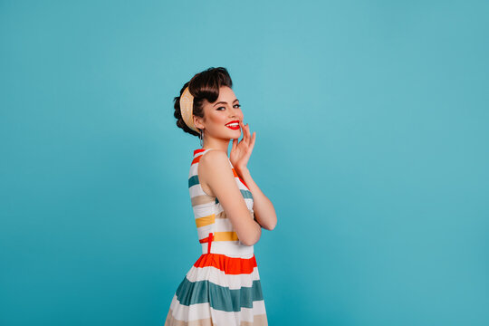 Carefree elegant woman posing in bright dress. Studio shot of stylish pinup girl laughing on blue background.