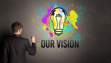 businessman drawing colorful light bulb with OUR VISION inscription on textured concrete wall, new business idea concept