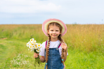 A little girl in a hat holds a bouquet of flowers on a sunny day.