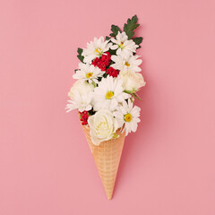 Flat-lay of waffle sweet cone with flowers over pastel light pink background, top view. Spring or summer mood concept, square crop.