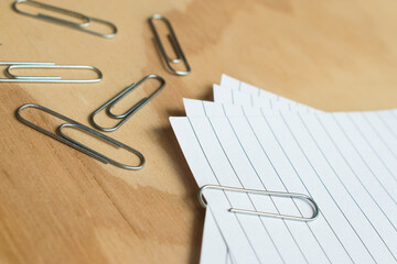 Metal paper clips and colorful  push pins with some sheets on a wooden table 