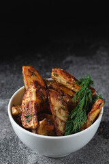 Delicious baked country potatoes with dill and spices in a white bowl on a dark stone table