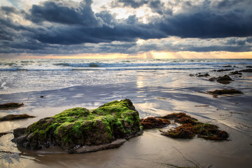 Light rays illuminate the Pacific Ocean beneath dark storm clouds at Crystal Cove State Park in Laguna Beach, California.