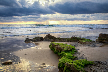Light rays illuminate the Pacific Ocean beneath dark storm clouds at Crystal Cove State Park in Laguna Beach, California.