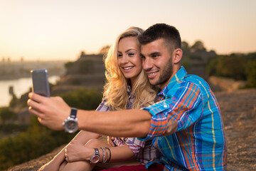 Romantic couple smiling and enjoying beautiful day in nature by the river. Young lovers taking selfies and having fun outdoors at sunset