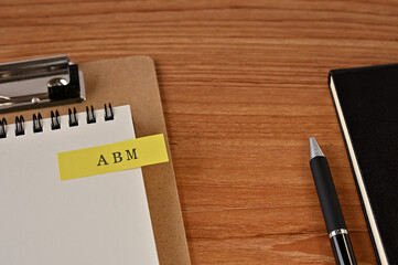 There is a notebook, a pen, and a clipboard with a sticky note stuck to it that says ABM written on it. It was an abbreviation for Account Based Marketing.