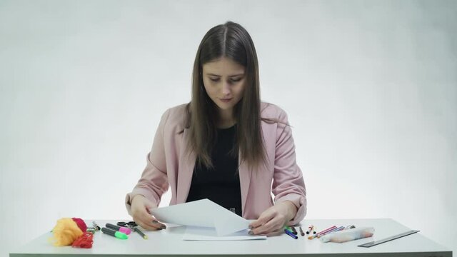 Attractive young woman makes a paper plane at the table in a white studio