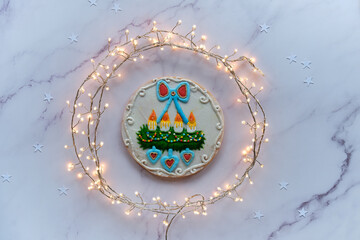 Gingerbread decorated with advent wreath with candles and hearts. Creative traditional gifts for children. Christmas flat lay with snowflakes, garland of lights on marble table.