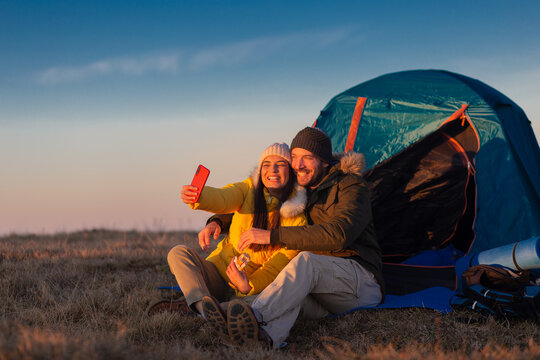 Portrait of a young couple taking a selfie with a phone in the mountains next to their tent.
