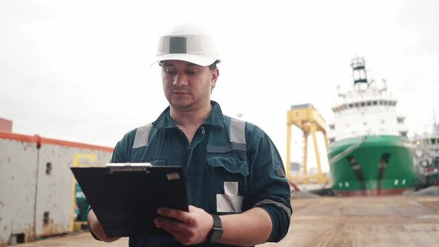 Marine Deck Officer or Chief mate on deck of offshore vessel or ship doing check and filling checklist. Paperwork at sea. Ship is on background