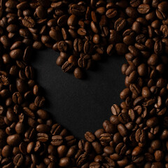 Fresh roasted coffee beans closeup on black stone background. Place for text in the shape of a heart. Top view, flat lay with copy space